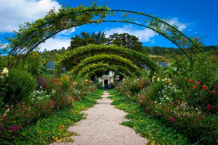 Flower-lined gravel path with green arched trellises leading to Monet's house in Giverny gardens