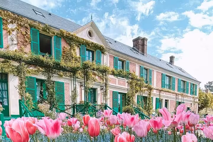 Claude Monet's pink house with green shutters and climbing vines surrounded by pink tulips in Giverny, France