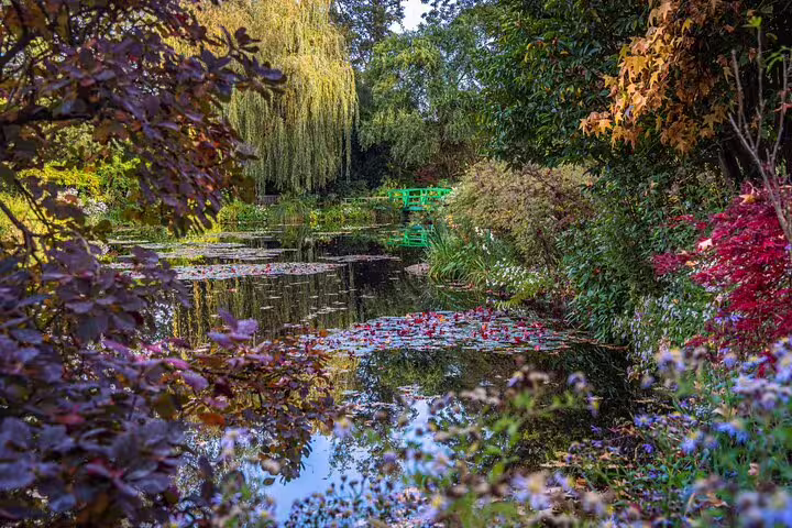 Monet's water lily pond with green Japanese bridge surrounded by colorful autumn foliage in Giverny