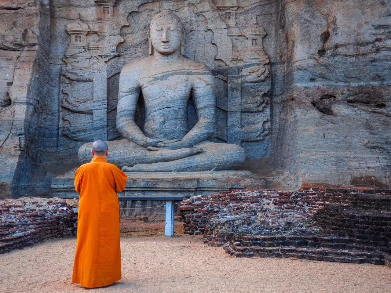 Monk in orange robe admiring ancient rock-carved Buddha statue at Gal Vihara, Polonnaruwa, Sri Lanka tour.