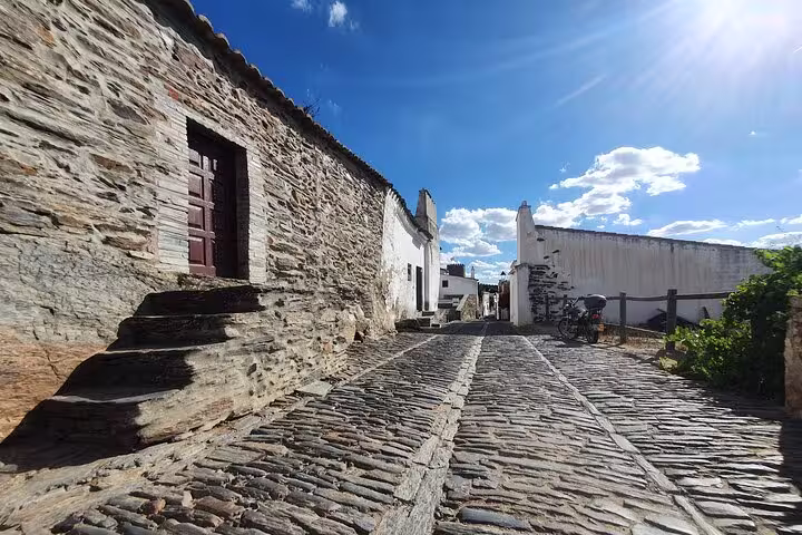 Scenic cobblestone street in Monsaraz with rustic stone buildings under a bright blue sky, featured in Evora & Monsaraz tour.