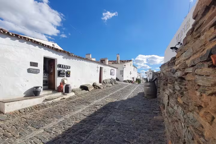 Charming cobblestone street in Monsaraz, Portugal, lined with whitewashed buildings under a bright blue sky.