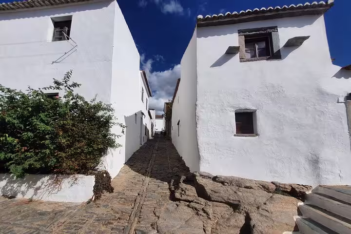 Charming narrow cobblestone street flanked by whitewashed houses under a clear blue sky in Monsaraz, Portugal.