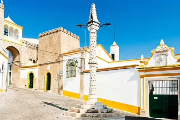 Historic street scene in Monsaraz, Portugal, featuring traditional architecture and a pillory under a clear blue sky, ideal for a guided day tour.