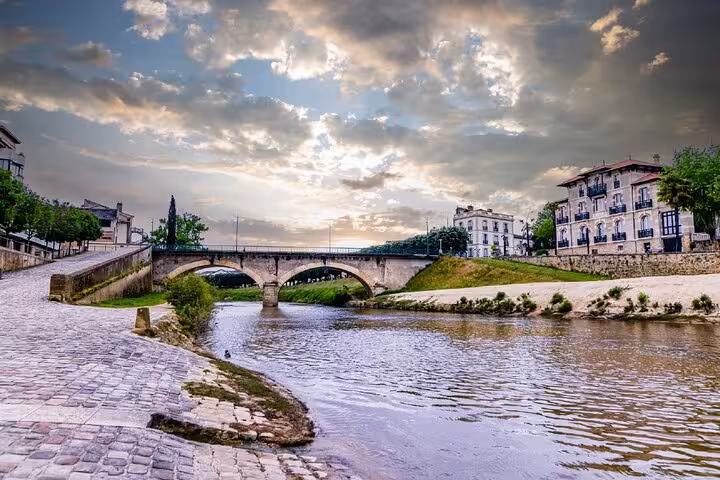 Stone arched bridge over a calm river in Mont de Marsan with historic buildings and cobblestone riverbank