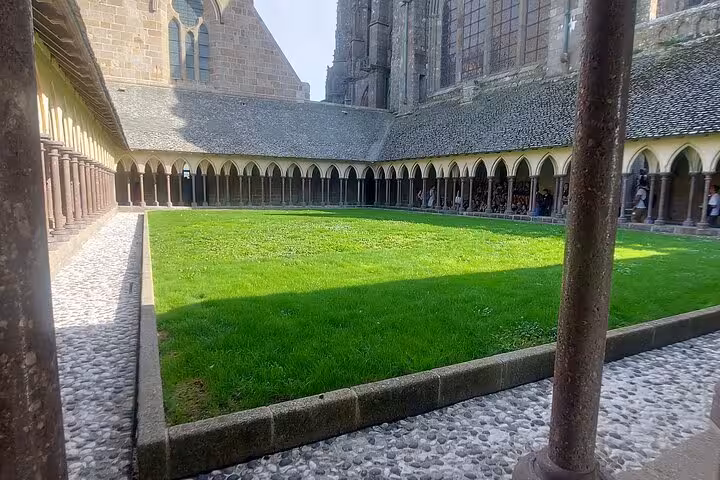 Mont Saint-Michel abbey cloister courtyard with arches and green lawn, visited on small-group day trip by luxury van