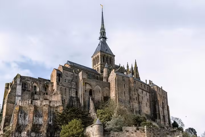 Mont-Saint-Michel abbey perched on rocky island with Gothic spire against cloudy sky, Normandy France