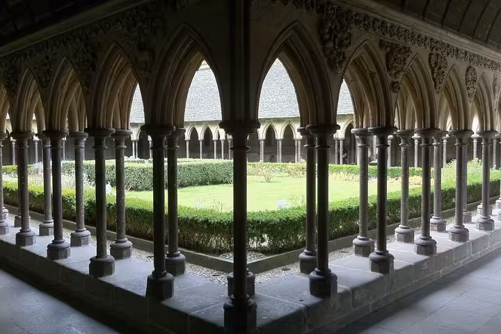 Gothic cloister arches and garden at Mont Saint-Michel Abbey, visited on small group day tour with luxury van