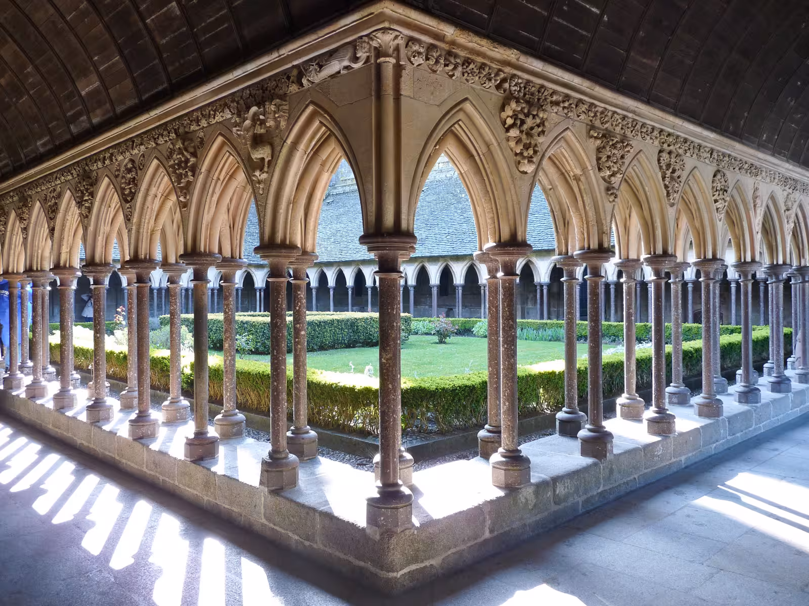 Gothic cloisters with ornate arched columns and garden courtyard at Mont Saint Michel abbey