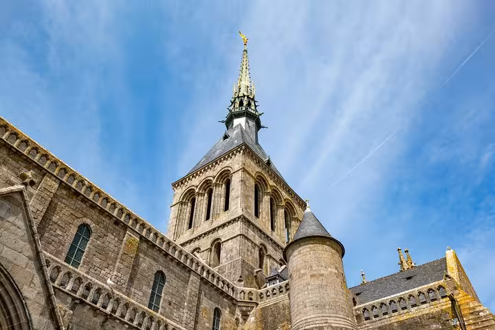 Gothic spire and stone tower of Mont-Saint-Michel abbey against blue sky, Normandy France