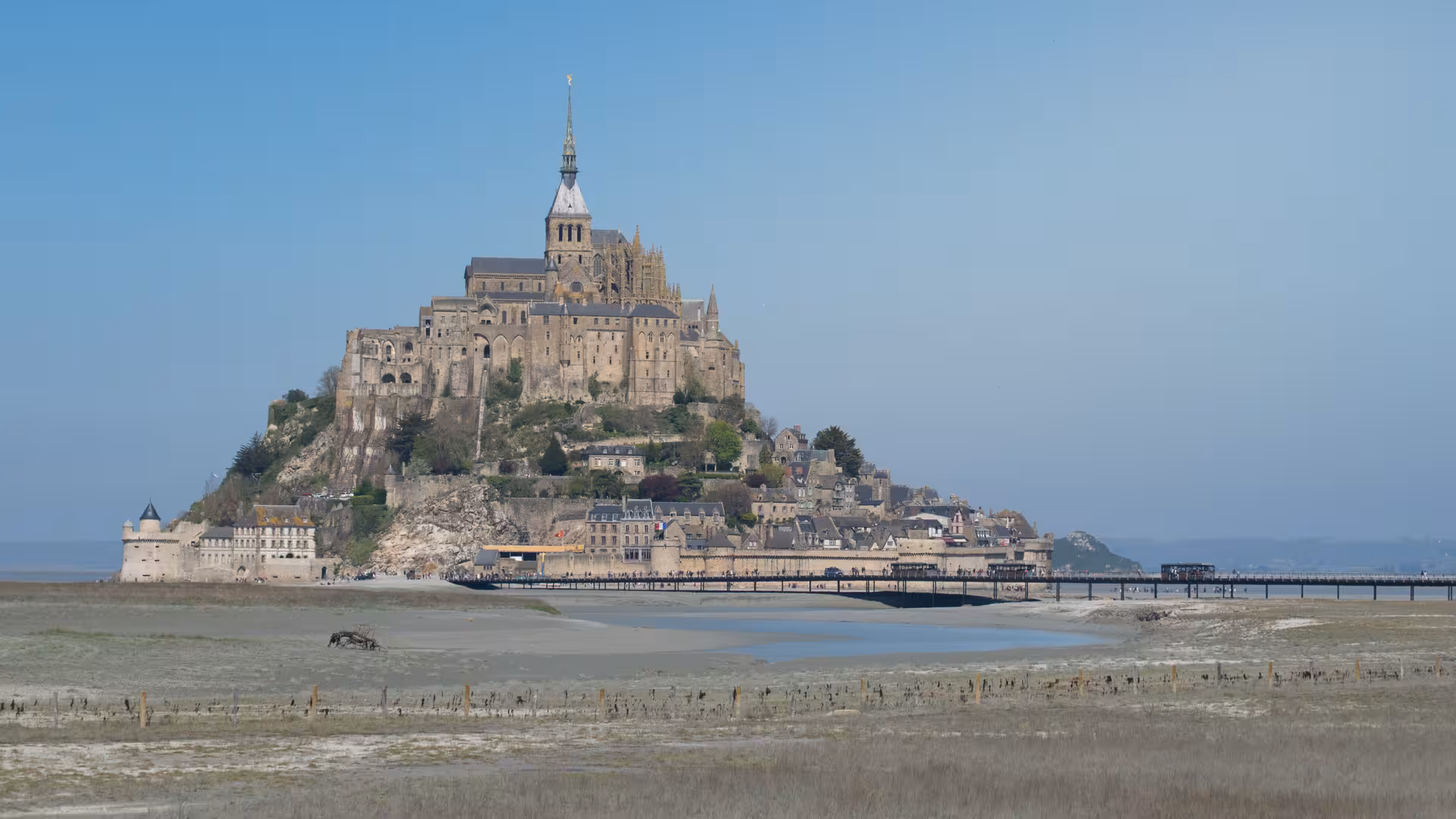Mont Saint-Michel island abbey rising above tidal flats with pedestrian bridge at low tide, Normandy France