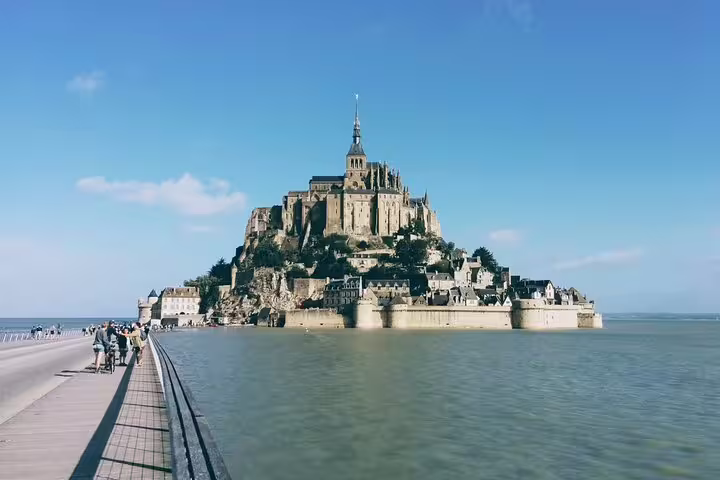 Mont Saint Michel island abbey rising above calm tidal waters with causeway walkway in foreground