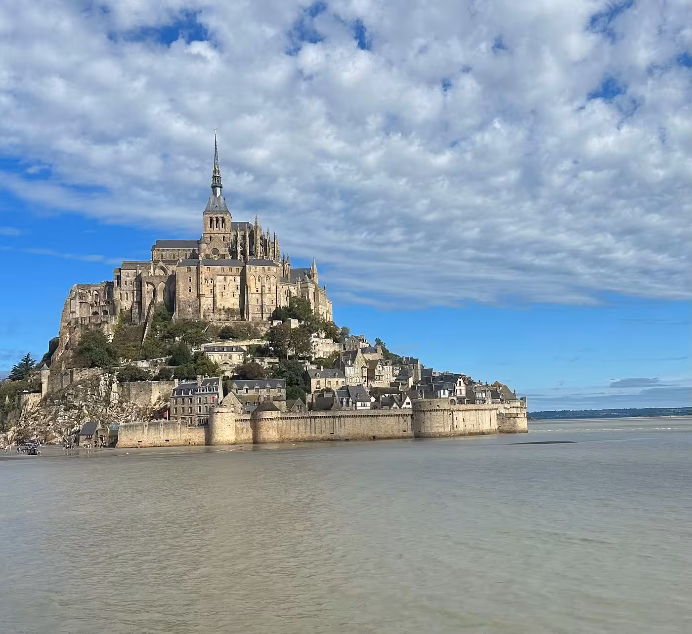 Mont-Saint-Michel island abbey rising above tidal flats with medieval village walls and Gothic spire against blue sky