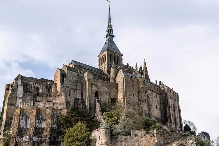 Mont-Saint-Michel abbey perched on rocky island with gothic spire against cloudy sky, Normandy France