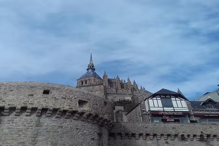 Medieval stone ramparts and abbey spire of Mont-Saint-Michel with Le Cheval Blanc hotel nearby