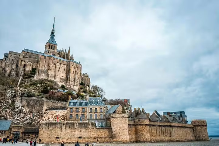 Mont Saint Michel abbey perched on rocky island with medieval walls and stone buildings below under cloudy sky