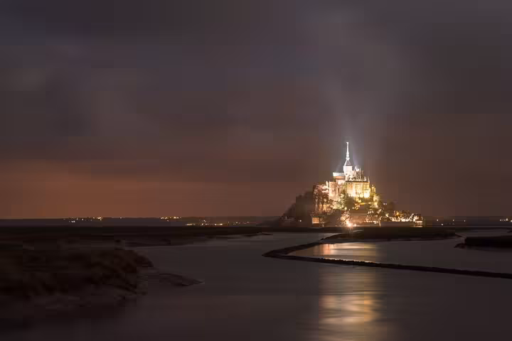 Mont Saint Michel abbey illuminated at night over tidal flats, Normandy small group day trip by luxury van