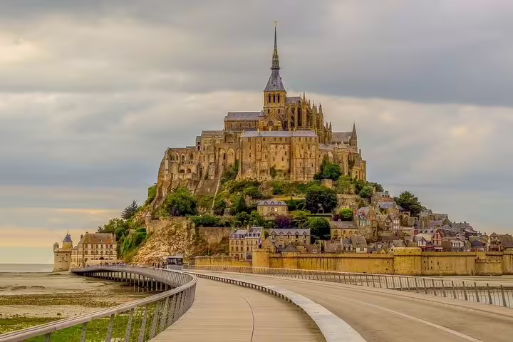 Mont Saint-Michel island abbey with causeway approach under cloudy skies, Normandy France