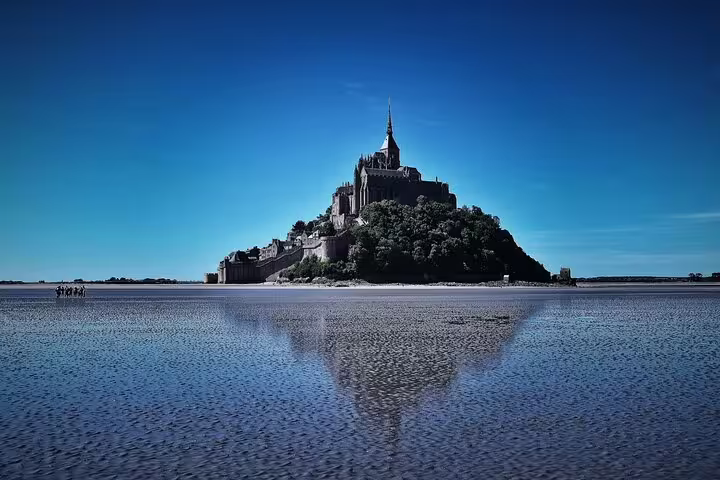Mont Saint Michel island abbey rising above tidal flats under clear blue sky, Normandy, France