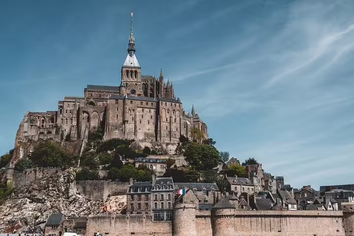 Mont Saint Michel abbey and village perched on rocky island with French flag under blue sky