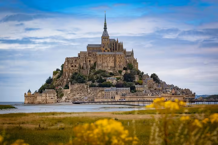 Mont-Saint-Michel abbey rising dramatically from tidal island with yellow wildflowers in foreground, Normandy France