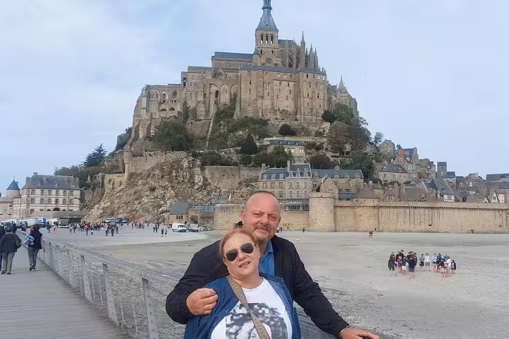 Travelers posing by Mont Saint Michel abbey and ramparts, memorable photo stop on small group luxury van day trip