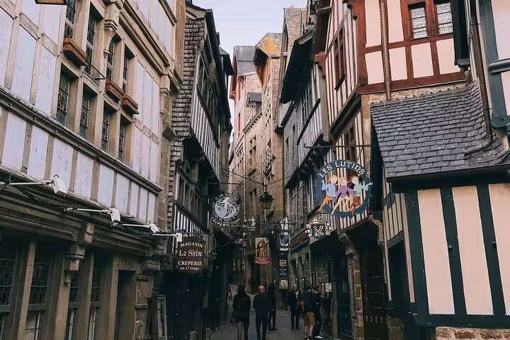 Narrow medieval street with half-timbered buildings and shop signs at Mont-Saint-Michel village