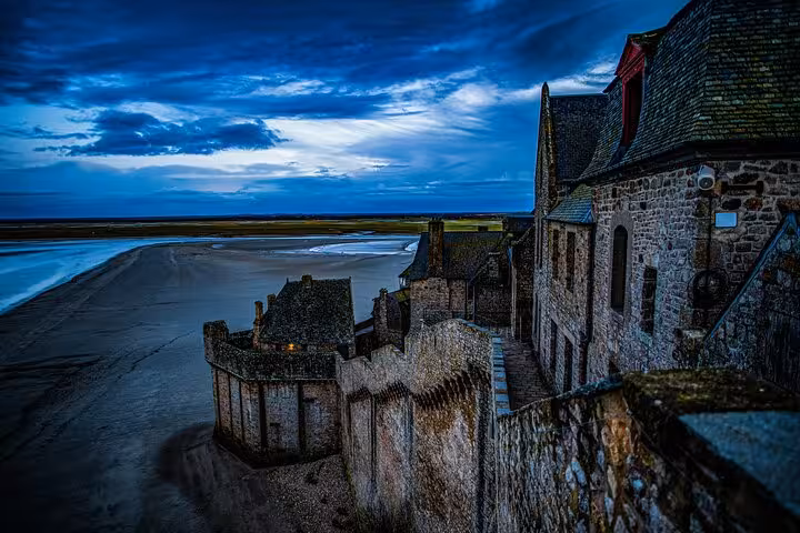 Stone walls and medieval buildings of Mont-Saint-Michel at dusk with tidal flats visible below