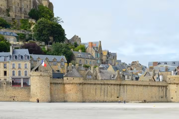 Medieval stone walls and buildings of Mont-Saint-Michel with French flag, viewed from the tidal flats