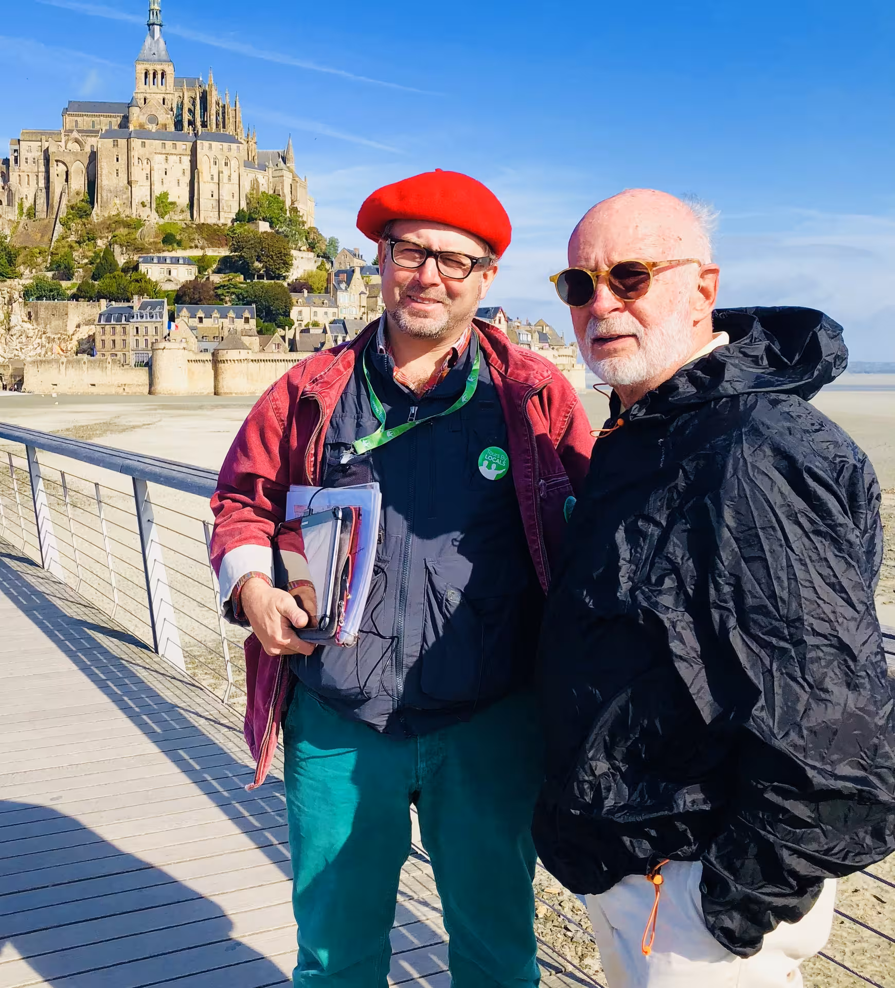 Tour guide in red beret with visitor on boardwalk in front of Mont Saint-Michel, Normandy France