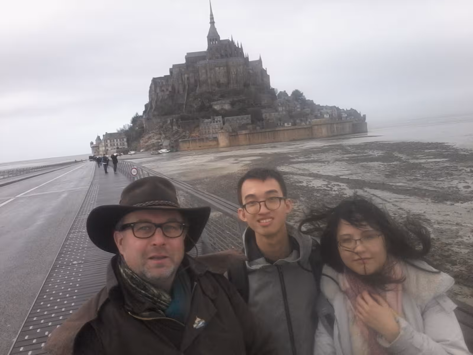 Three tourists taking a selfie on the causeway bridge leading to Mont Saint-Michel, Normandy, France