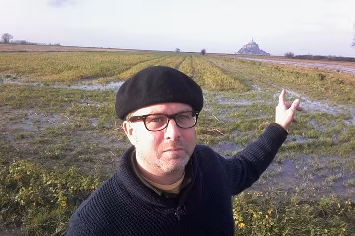Guide pointing toward Mont Saint-Michel from flooded farmland fields near St Malo