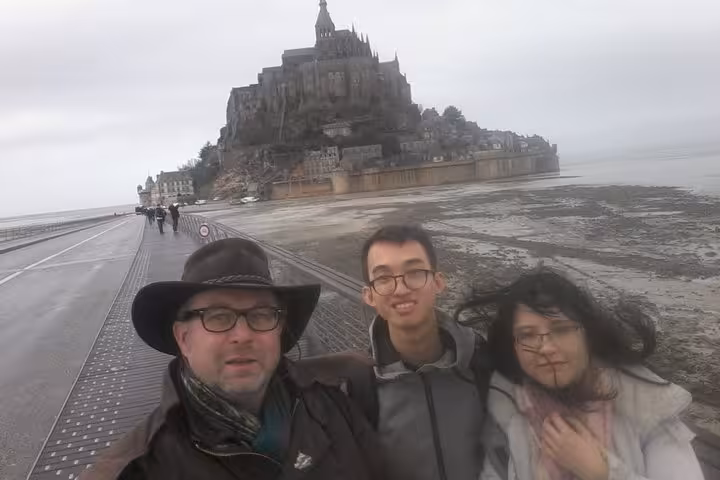 Three tourists taking a selfie on the causeway leading to Mont Saint-Michel on a cloudy day