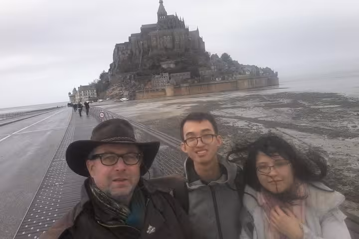 Three tourists taking a selfie on the causeway bridge with Mont Saint-Michel abbey in the background