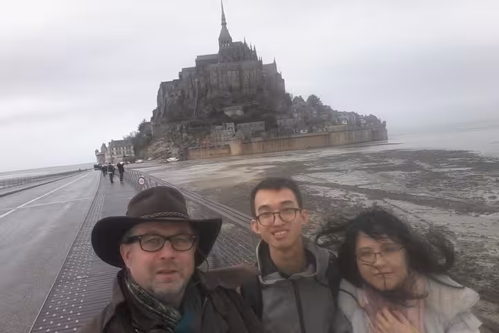 Three tourists taking a selfie on the causeway leading to Mont-Saint-Michel on a cloudy day
