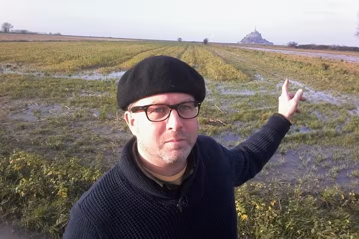 Guide pointing toward Mont Saint-Michel in distance across flooded farmland fields in Normandy