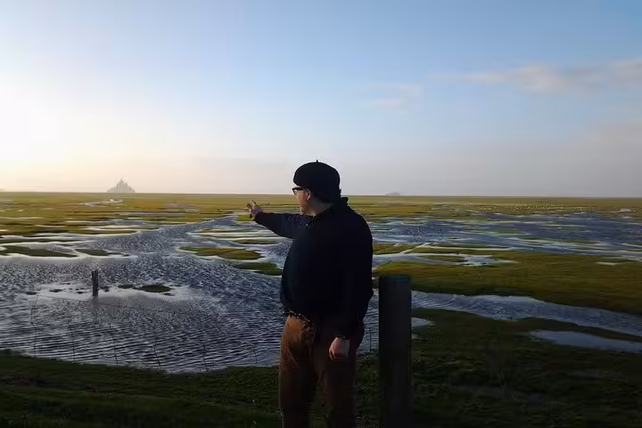 Tourist pointing toward Mont Saint-Michel across tidal flats during private tour from Cherbourg