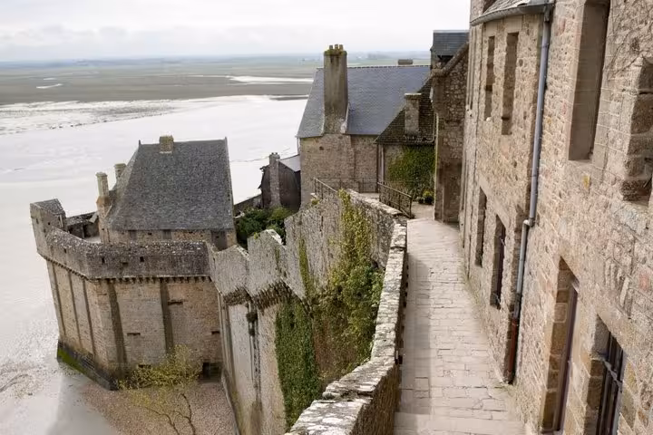 Narrow stone rampart walkway at Mont-Saint-Michel with tidal flats visible in the background