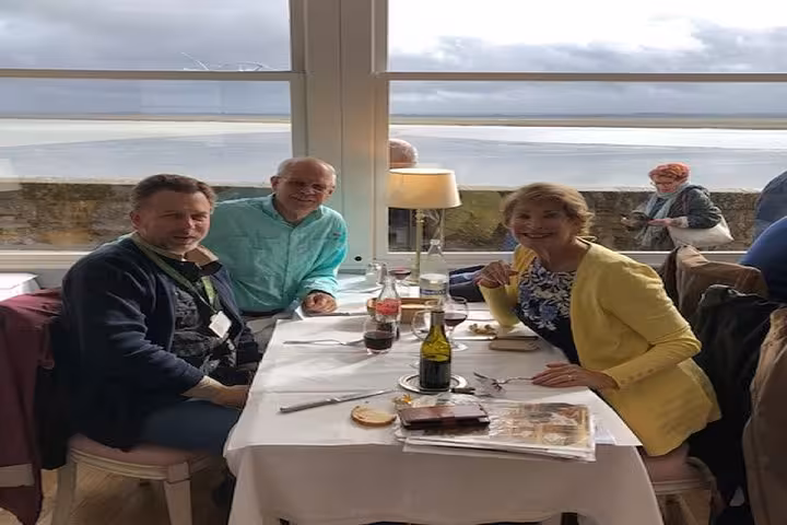 Three tourists dining at Mont Saint-Michel restaurant with scenic bay views through large windows