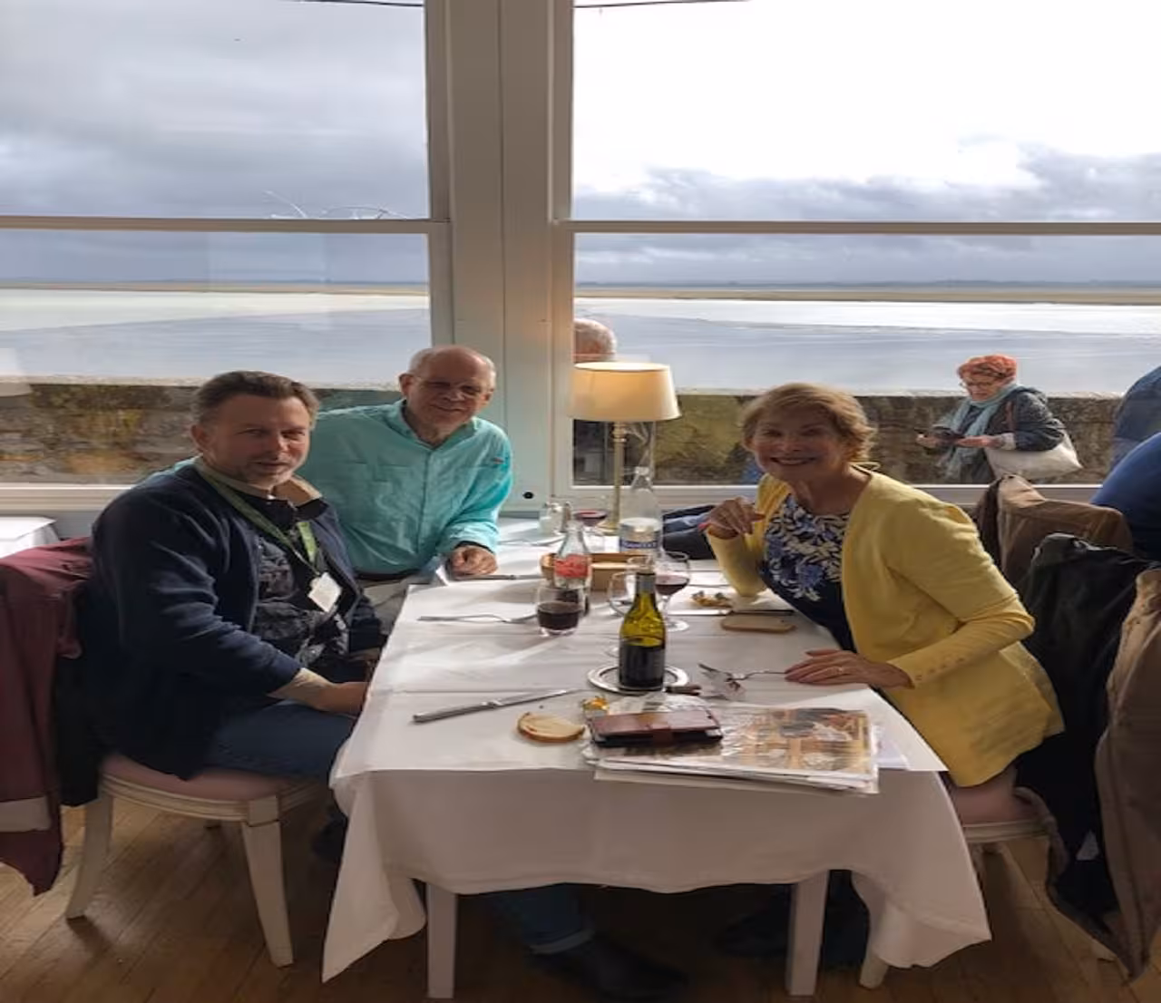 Three travelers dining at restaurant table with ocean view at Mont Saint Michel, Normandy France