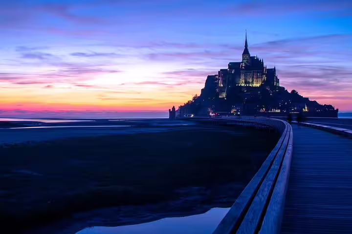 Mont Saint Michel illuminated at sunset with causeway leading to the tidal island in Normandy, France
