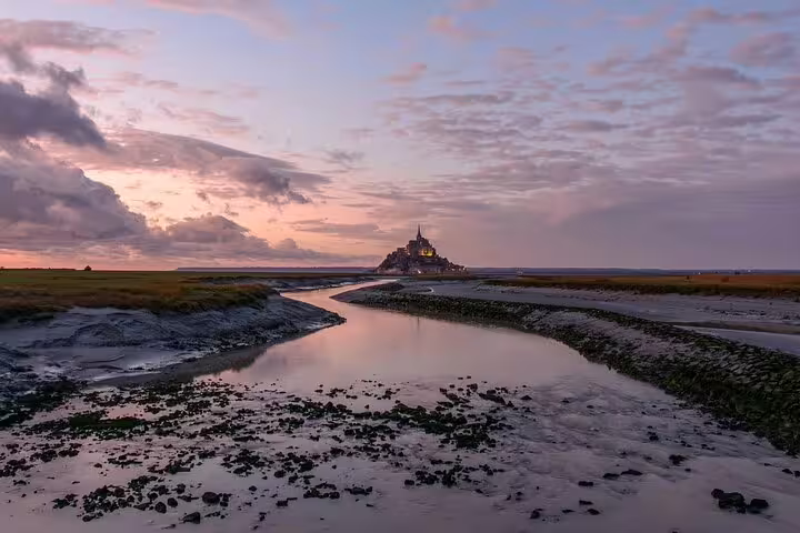 Mont Saint Michel illuminated at sunset with tidal flats and winding river in foreground, Normandy France