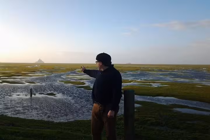 Tourist pointing toward Mont Saint-Michel across tidal marshes from Le Havre private tour