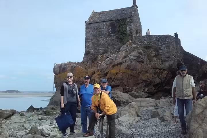 Tour group posing near ancient stone chapel on rocky coast at Mont-Saint-Michel