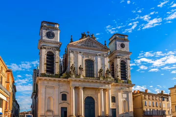 Baroque facade of a twin-tower cathedral with statues and clock faces in Montauban, France