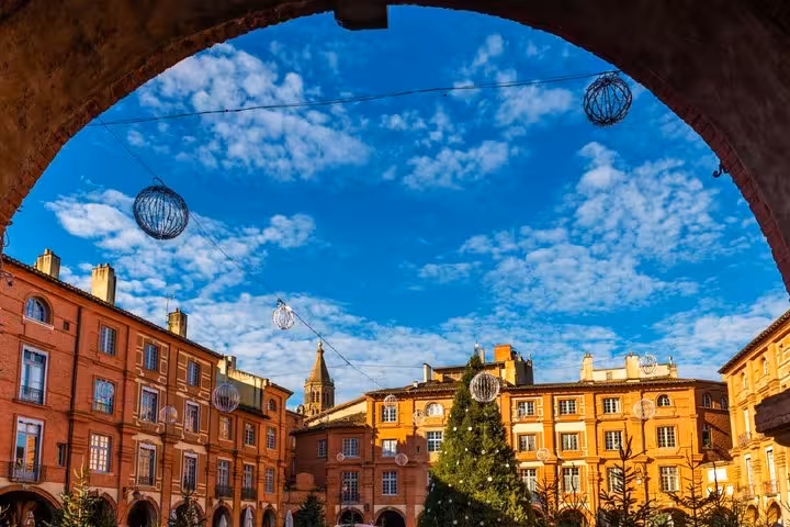 Montauban town square with red brick buildings, Christmas tree, and decorative orbs viewed through an arch