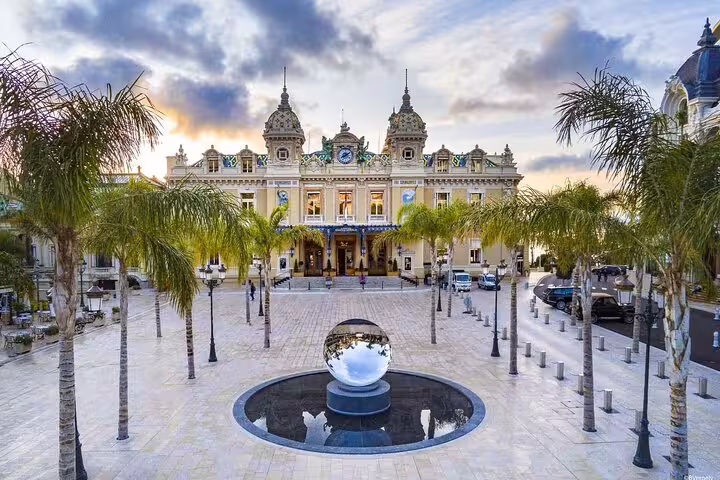 Monte Carlo Casino facade with palm trees and reflective sphere fountain at sunset, French Riviera