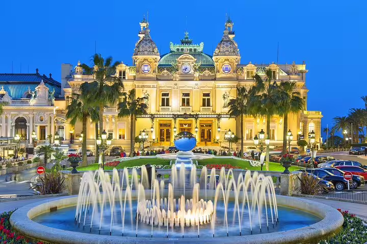 Monte Carlo Casino illuminated at dusk with fountain and palm trees, Monaco French Riviera
