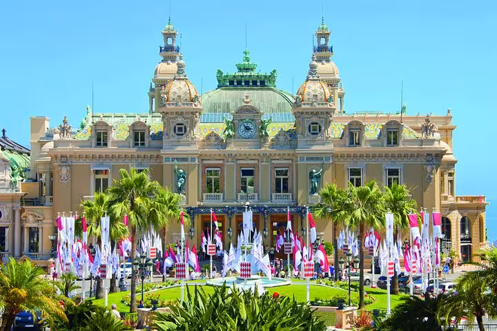 Monte Carlo Casino facade with ornate Belle Époque architecture, palm trees, and colorful flags in Monaco