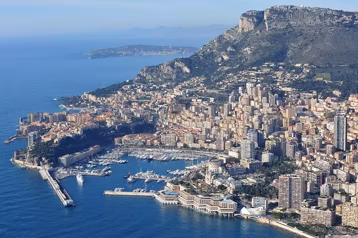 Aerial view of Monte Carlo's stunning coastline and marina with luxury yachts and mountainous backdrop.